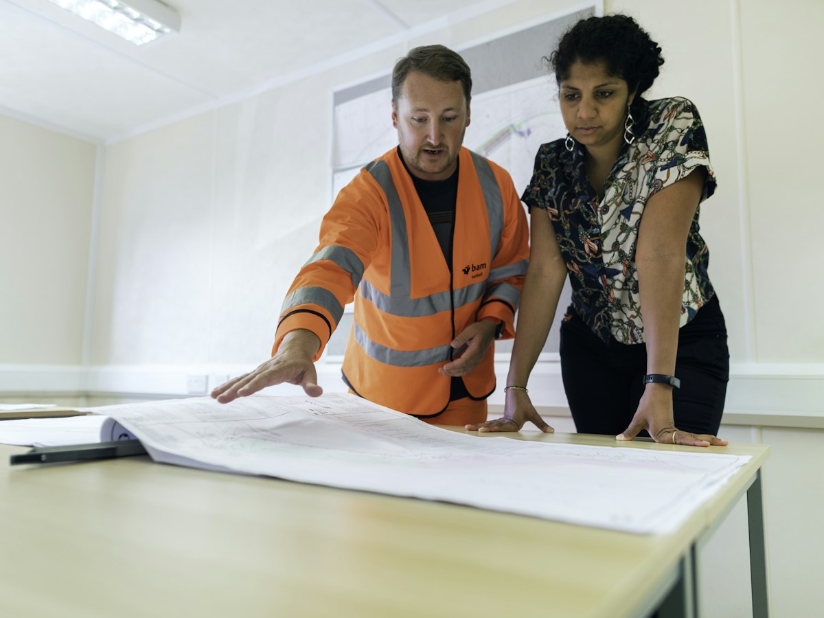 Two colleagues, one in a high-visibility vest, reviewing a large traffic control plan drawing